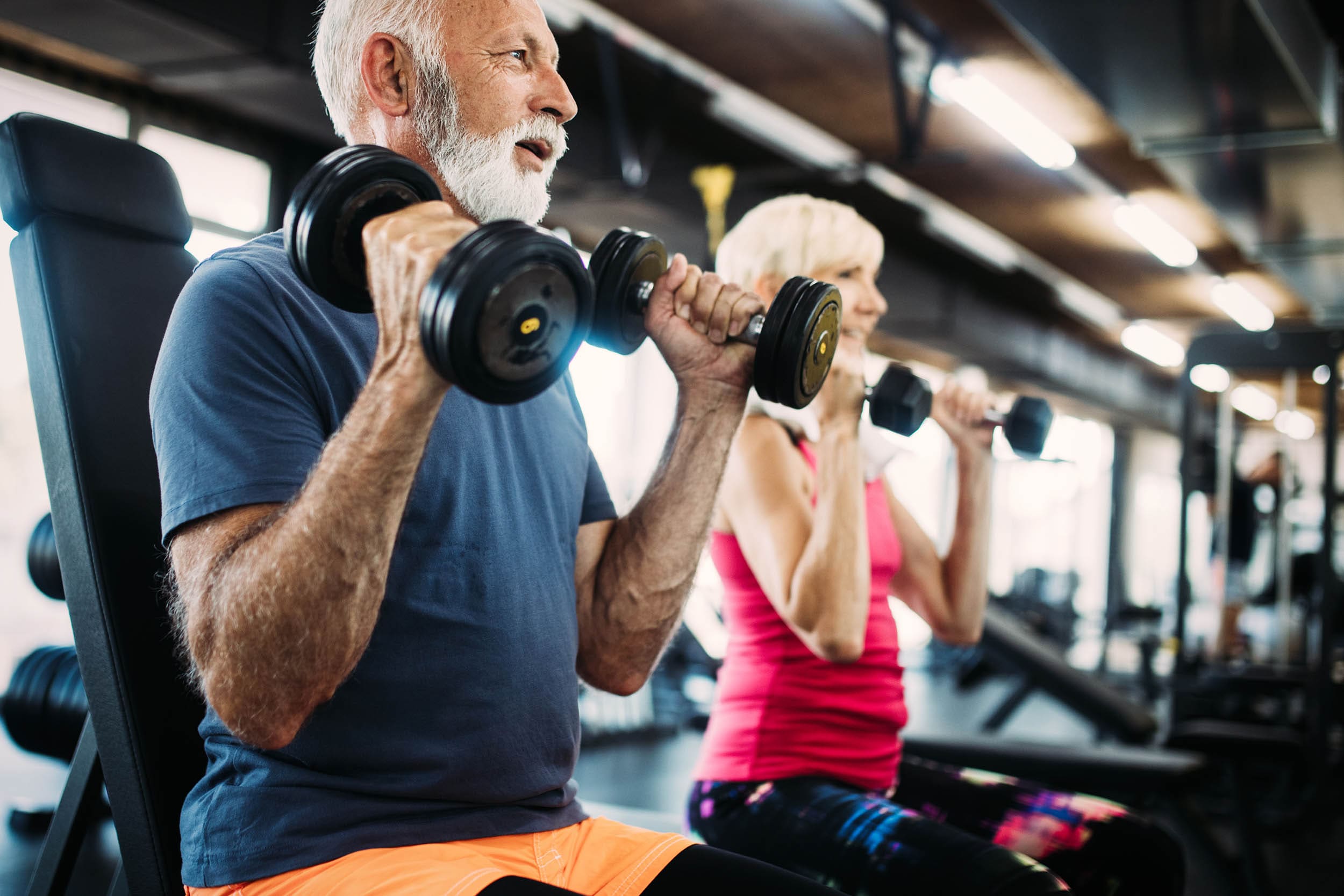 Senior fit man and woman doing exercises in gym to stay healthy